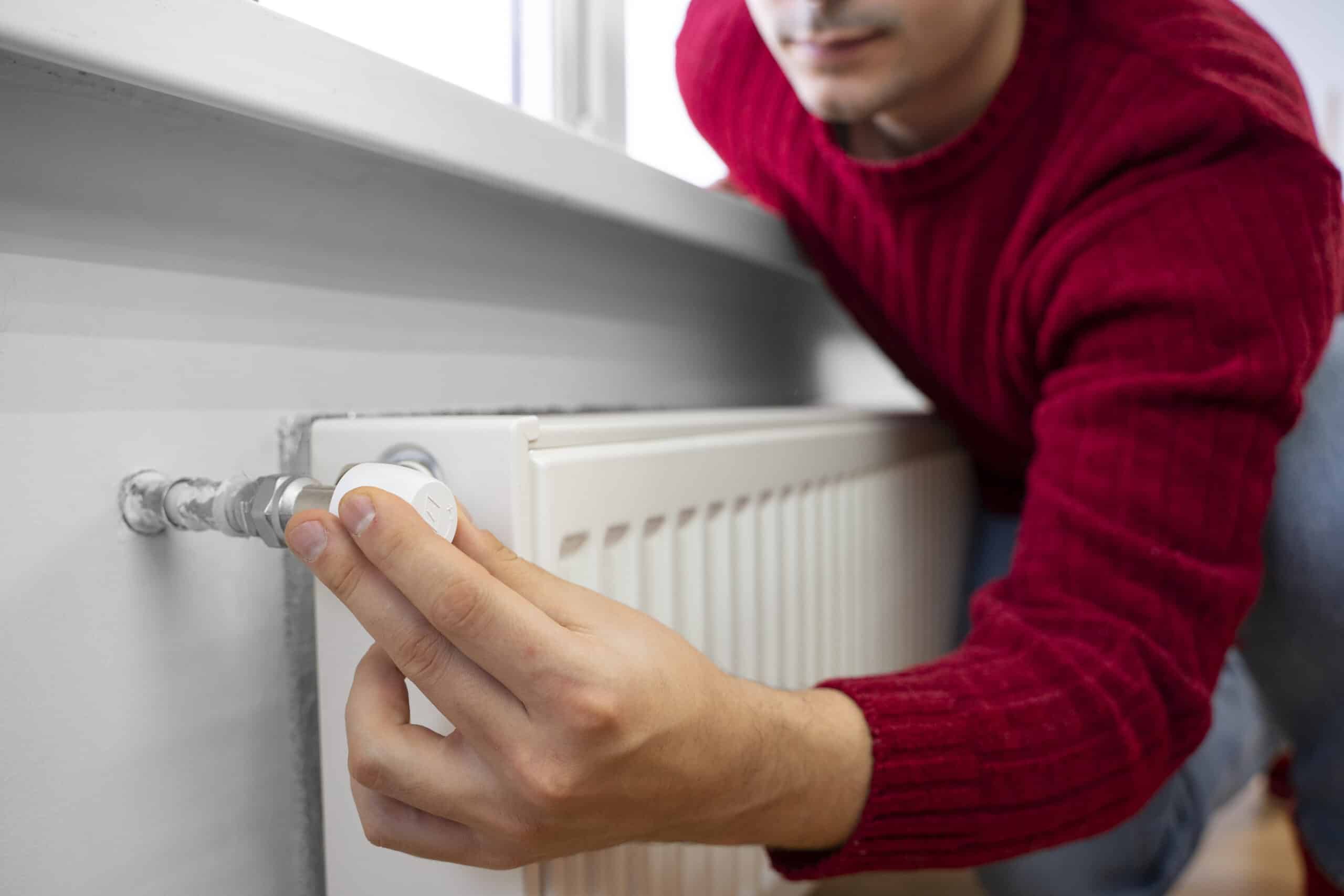 homme qui regle radiateur homme proche du radiateur qui essaie de régler la tête thermostatique